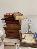 Photo showing the large wooden jewelry box with drawers and brass handles alongside other wood boxes and the metal jewelry stand.