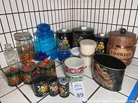 Overall view of assorted kitchen organizers including glass jars, tins with floral designs, plastic bowls, and a wooden cookie jar