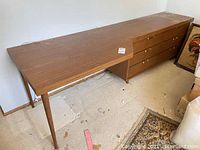 Full view of the long wooden desk showing the drawer cabinet corner and supporting legs.
