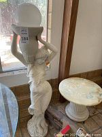 Overall view of plaster statue holding urn with plastic globe and adjacent round pedestal table
