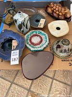 All items displayed together in cardboard box on floor, various ceramic, glass and wood decor items including vases, bowls, plates, candle holder, and glass sculpture.