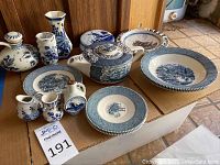 Full view showing Delft mini vases and pitchers with cork lids, liqueur bottle, and American dishes including plates and saucers on cardboard base