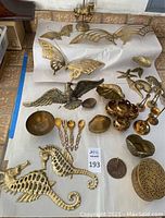 All brass decor items displayed on white paper on floor. Includes animals, butterflies, bowls, a lidded container, and flatware.