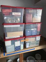 Six transparent bins with red lids stacked on bench
