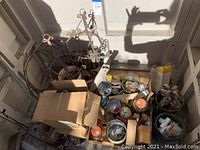 Wide shot showing assorted iron plant stands, various boxes, containers with small hardware and tools inside a storage corner.