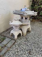 Two concrete stone lanterns side by side showing size difference and general condition outside against a wall.