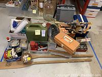 Overview of outdoor adventure gear including fishing rods, wooden oars, green cooler, fishing tackle boxes, and other equipment spread on floor