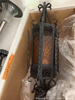 Photo of one iron pendant light fixture showing amber textured glass panels and decorative scrollwork