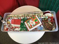 Top view of the plastic bin with assorted Christmas gift wrap supplies including rolls of wrapping paper, gift bags, ribbons, tape, and bows.