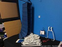 IKEA blue fabric folding shoe organizer with 10 compartments, a pile of white plastic hangers, black metal tie rack, white door hooks and laundry hooks on blue background.