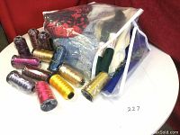 Bag containing assorted fabric pieces and 12 large spools of serger thread in various colors arranged on a white surface.