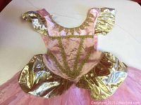 Pink and gold princess ball gown with gold glitter details and metallic puff sleeves shown on a white background.