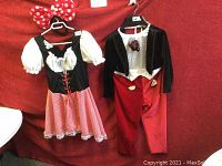 Two kids Halloween costumes hung against red background, Minnie Mouse on left, Mickey Mouse on right.