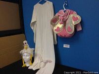 Full view of adult white rabbit costume hanging showing ears on headband and attached tail, infant pink butterfly costume with heart-decorated gold wings hanging on wall, and wacky chicken hat on mannequin head.