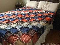 Full view of handmade rag quilt on bed with visible patchwork squares in orange, navy, beige and floral prints with ragged edges.