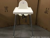 Front view of the white IKEA high chair showing one-piece molded seat, attached tray, and gray legs with rubber feet.