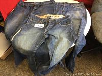 Three pairs of men's jeans laid flat showing front, different denim washes, size sticker on one