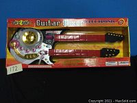 Full view of the electronic guitar mixer toy in its original packaging showing two red guitar necks and circular control with buttons and knobs.