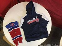 Photo of navy blue Montreal Canadiens hoodie with white shoulder accents and front pouch pocket, along with a red, white, and blue Montreal Canadiens toque showing the team logo.