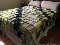 Top view of quilt spread on bed showing rag-style patchwork in various colors including yellow, green, black, and beige.