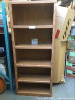 Full view of tall oak book shelf showing five shelves and natural wood finish.