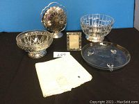 Full lot view showing all items: anniversary cake plate, two glass bowls, foldable three tier cookie tray, picture frame, and folded embroidered cloth