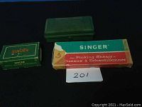 Photo of three boxed Singer sewing machine accessories: pinking shears box, green attachment case, and small green box.