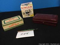 Photo featuring the Singer Button Holer box, the Singer Automatic Zigzagger box, and the maroon sewing cube/tool case together on a blue background.