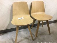 Front view of two light oak wood chairs with molded curved seats and solid angled legs