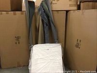 White rectangular foam block with a tapered edge, positioned in front of stacked cardboard boxes.