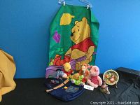 Wide view of the collection showing Winnie the Pooh garden flag, five stuffed toys, Pooh tote bag, Kangaroo and Roo wall plate, and figurine