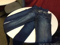 Two pairs of women's jeans laid flat on a round white table: one Guess boot cut and one Hollister skinny