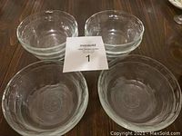 Four clear Pyrex glass bowls arranged with a MaxSold lot number card in the center, showing their round shape and transparency.