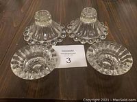 Four clear lead crystal candle holders displayed on a wooden surface, showing two pairs with different base shapes and edge designs.