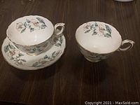 Two teacups and one saucer with floral design and gold trim on a dark wood surface
