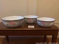 Three nested enamel metal bowls with floral decoration shown side by side on wooden surface
