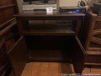 Front view of wooden TV stand showing top surface and middle shelf with items on top.