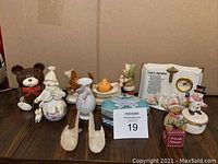 Wide view of assorted small figurines and decorative ceramic pieces including snowmen, bears and birds displayed on a wooden surface.