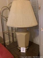 Single beige ceramic table lamp with a hexagonal base and pleated beige fabric lampshade, positioned on a dark wood surface.