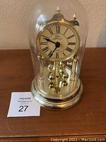 Front view showing the brass Anniversary clock under glass dome, Roman numeral dial marked Elgin Anniversary, and rotating brass pendulum balls.
