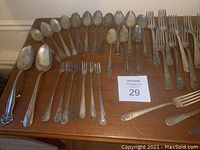Photo showing large spoons, various forks, including smaller serving forks, and two serving spoons arranged on a wooden surface.