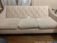 Front view of the beige three-person sofa showing the full length and cushioned seating.