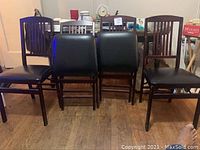 Four dining chairs arranged with two wooden slat back chairs on the ends and two black cushioned folding chairs in the middle, wooden floor visible.