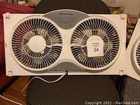 Photo of one Comfort Zone dual fan window fan showing dual circular fan blades with grille, central control panel and white plastic casing.