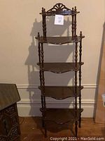 Front-facing photo showing the entire five-tier antique wood shelving unit with carved crest and spindle supports.