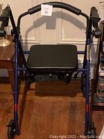 Front view of the blue rollator walker showing padded black seat, adjustable handles, wheels, and hand brakes.