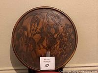Photo of a circular carved wooden tray with African folk art figures and a small MaxSold lot tag.