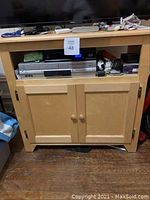 Front view of light wood TV stand showing open shelf with electronics and closed cabinet doors.