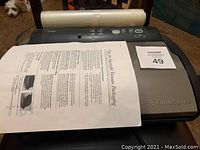 FoodSaver vacuum sealing machine showing control buttons and top panel with instruction sheets and vacuum rolls on top.