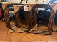 Three dark wood picture frames with cardboard corner protectors placed on a wooden floor, background with household items.